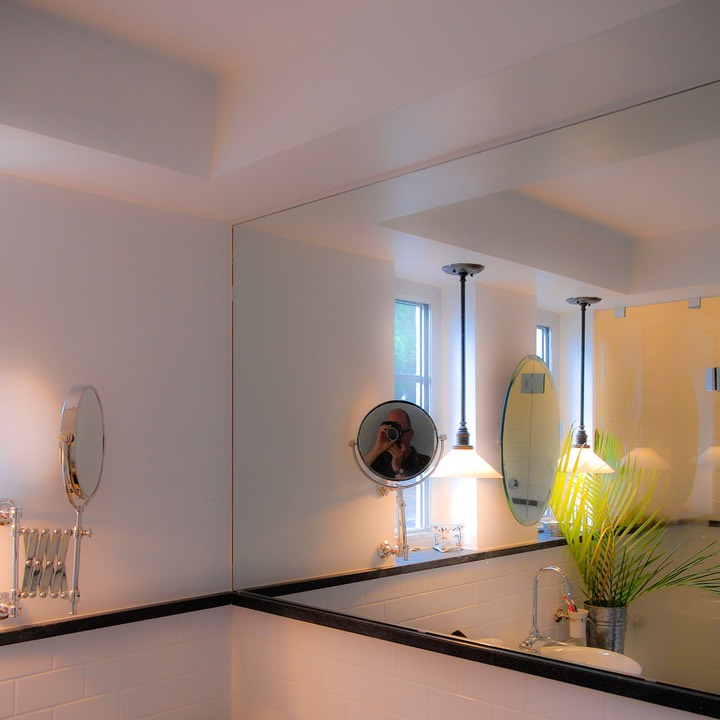 circular telescoping mirror catches the photographer's reflection off a larger wall of mirror that doubles the size of the bathroom