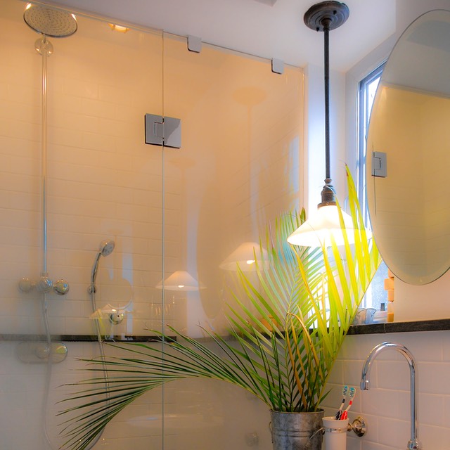 palm leaves in corrugated steel vase set against shower glowing softly through its minimal glass wall